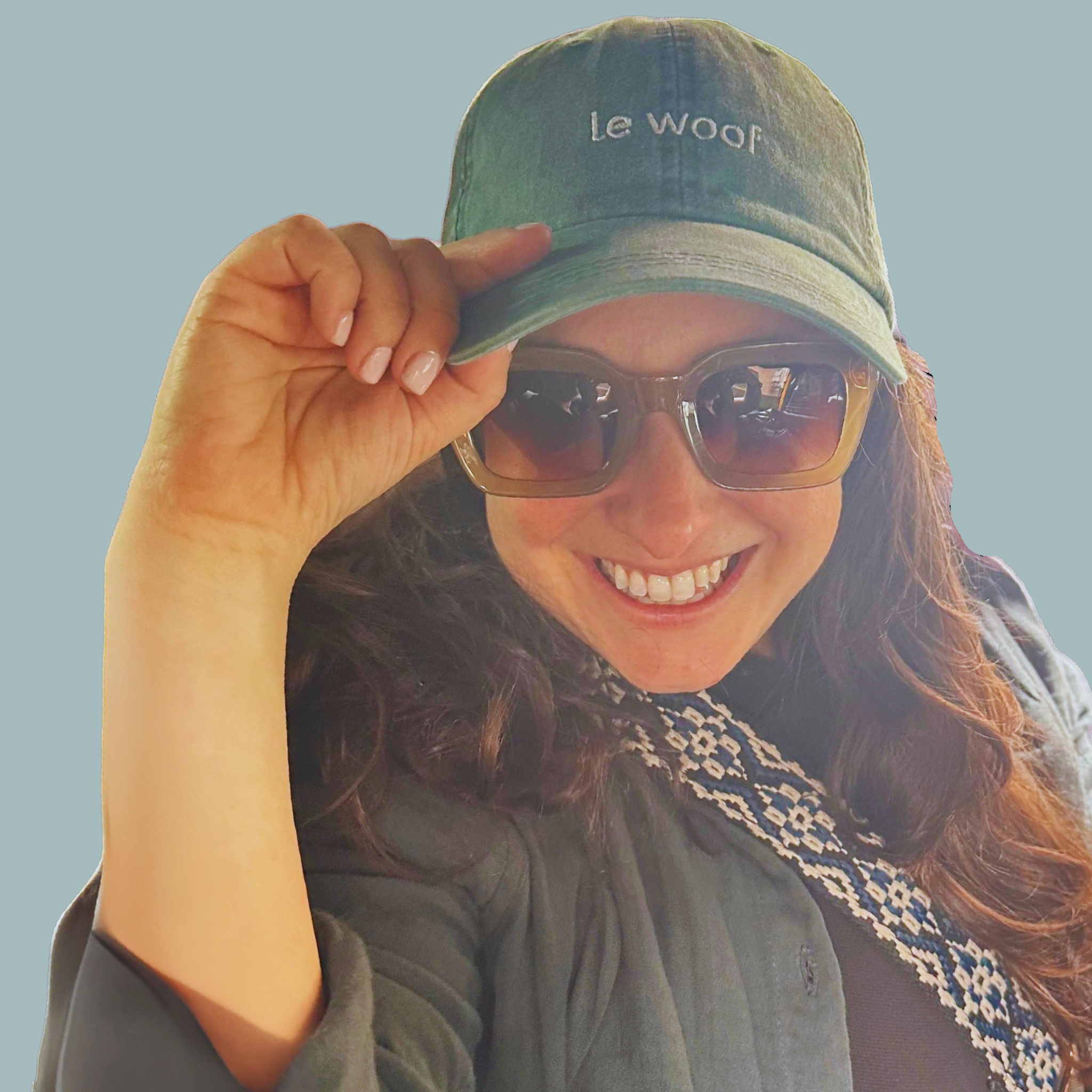 Picture of Le Woof Founder, Hila Raz Harris, wearing Le Woof Baseball Cap and smiling on a light green, sage toned background